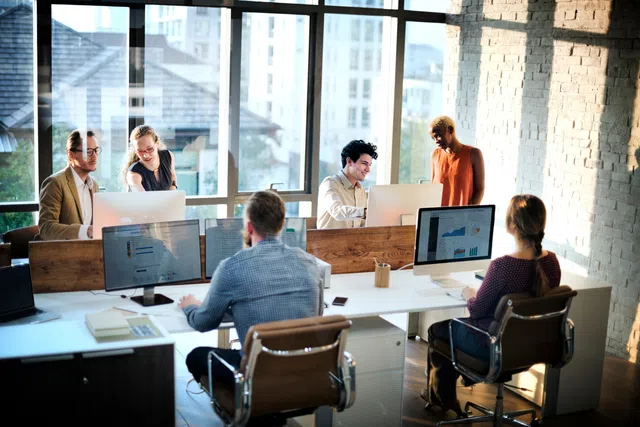 Team collaborating in a modern office with large windows and computer screens displaying data.