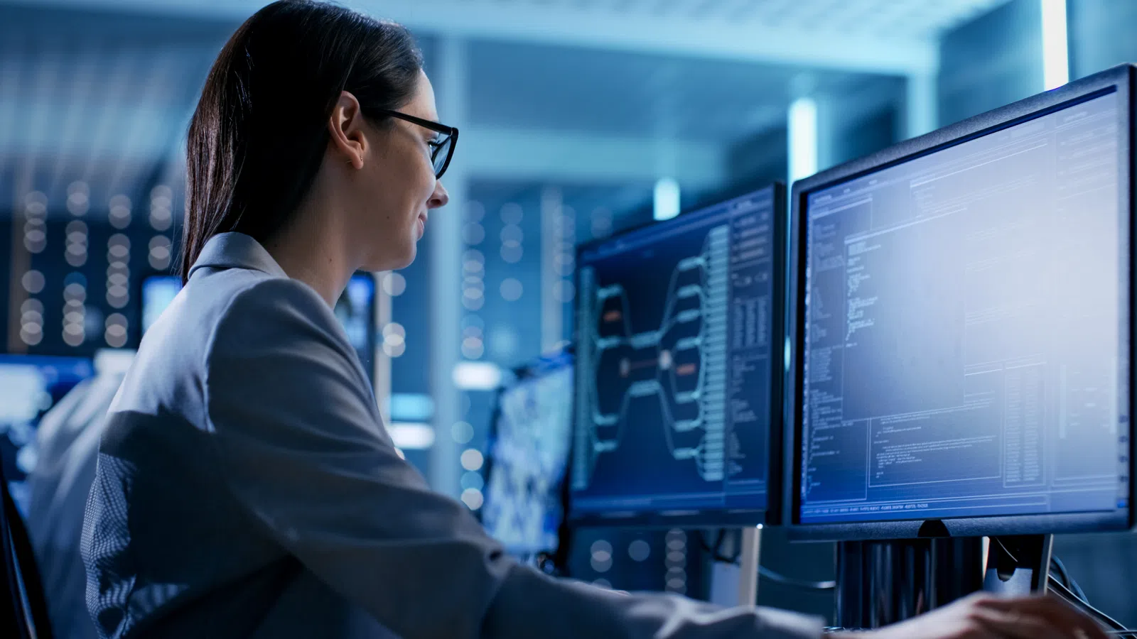 Professional woman working on multiple computer screens in a modern office environment.