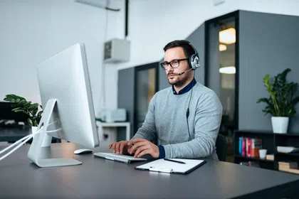 A focused man wearing headphones works on a computer in a modern office setting.