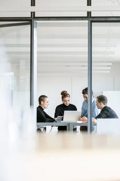 Four professionals collaborating over a laptop in a modern office setting.