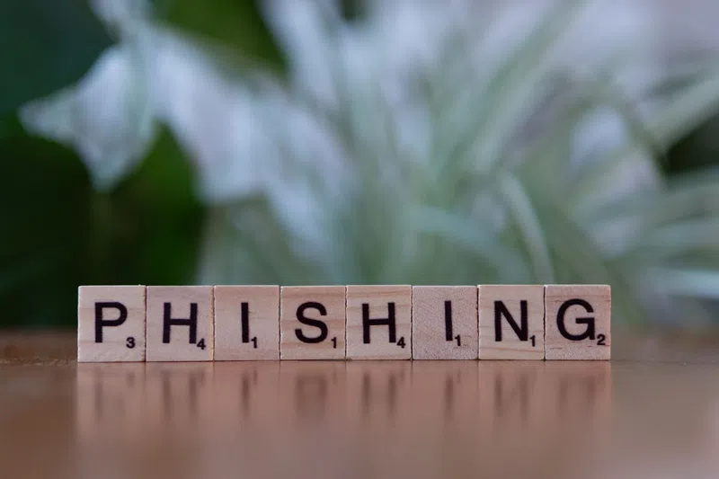 Scrabble tiles spelling the word PHISHING on a wooden surface with blurred green background.